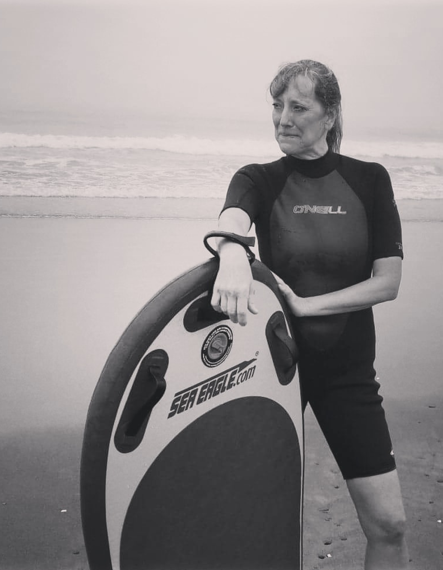 Person in a wetsuit holding a Sea Eagle bodyboard on a beach